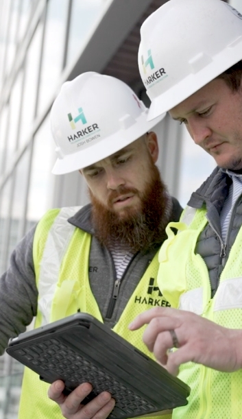 Two male construction workers with Harker hard hats looking at a tablet